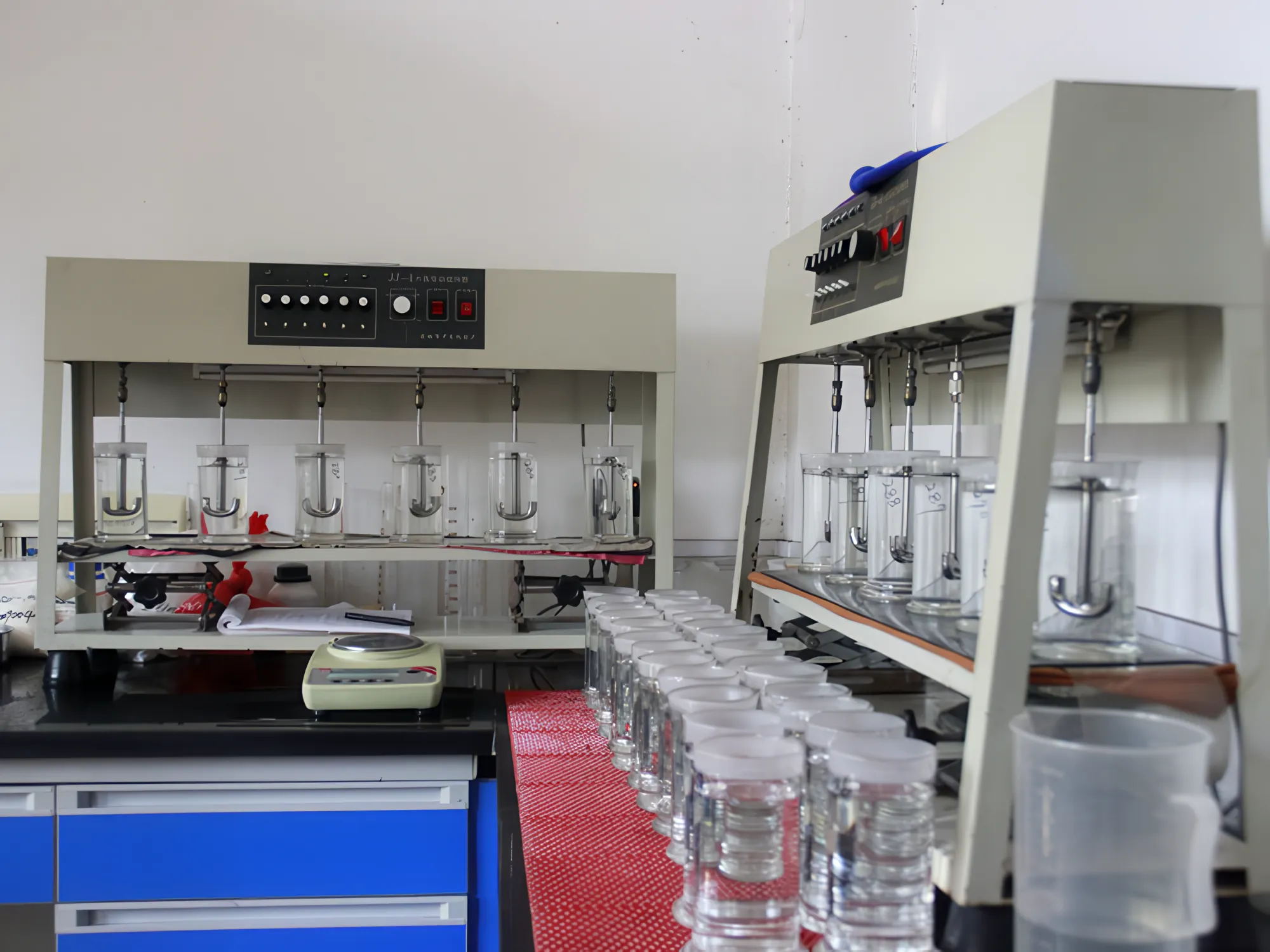 Two multi-position laboratory stirrers with rows of glass beakers on a bench in the quality-control laboratory