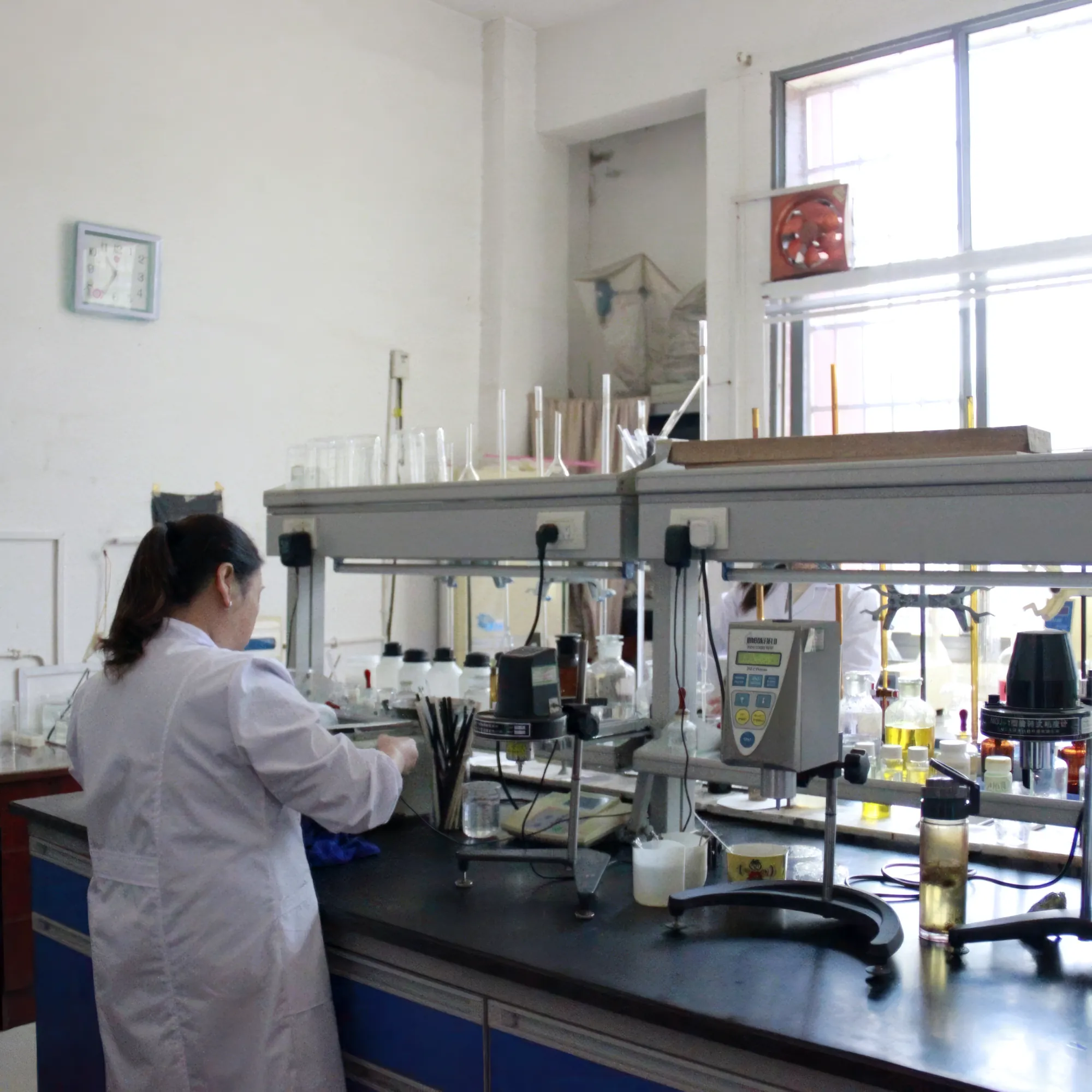 Technician in a white coat at a laboratory bench with stirrers, instruments, beakers and reagent bottles