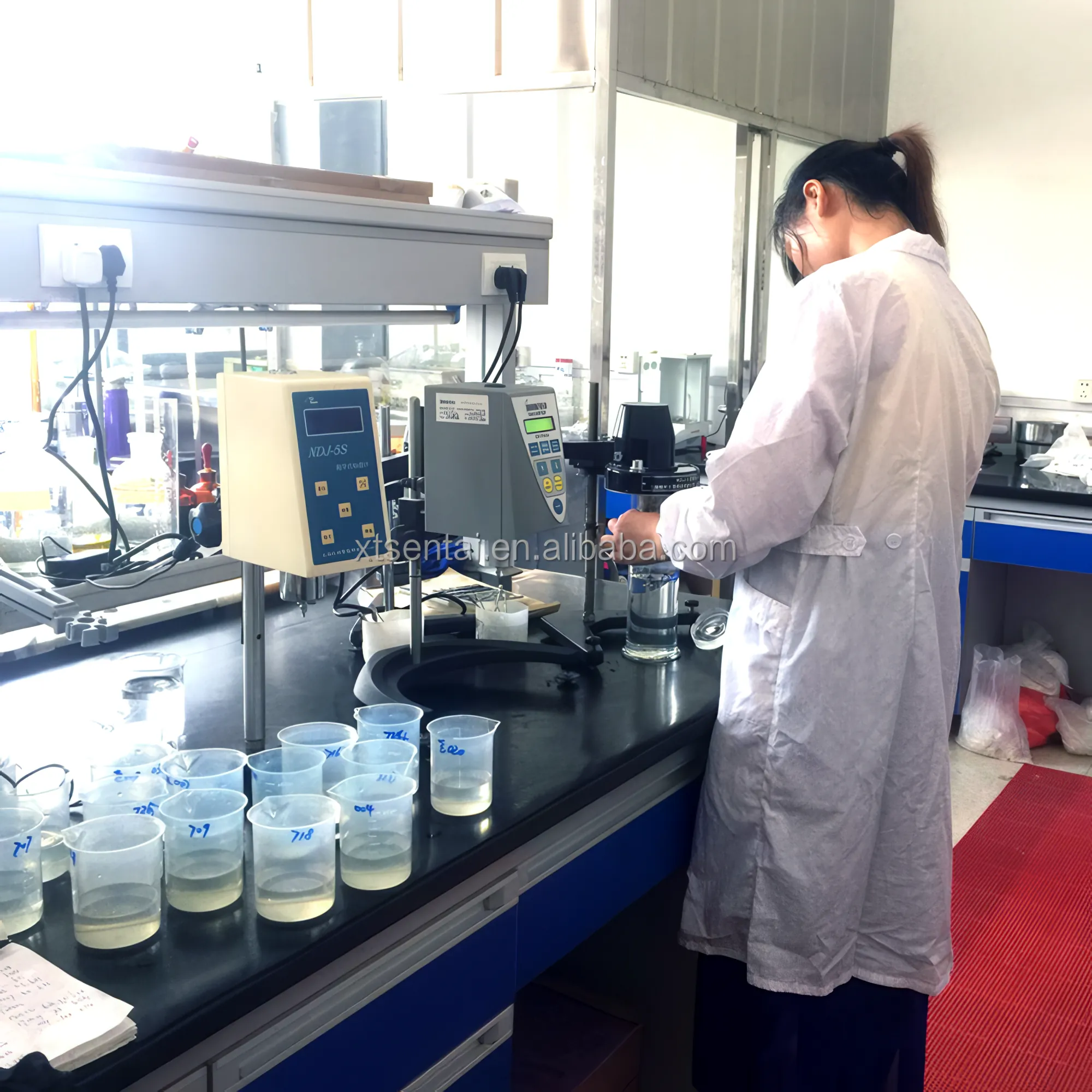 Technician in the Sentai laboratory at a bench with two viscometers and rows of beakers holding CMC sample solutions