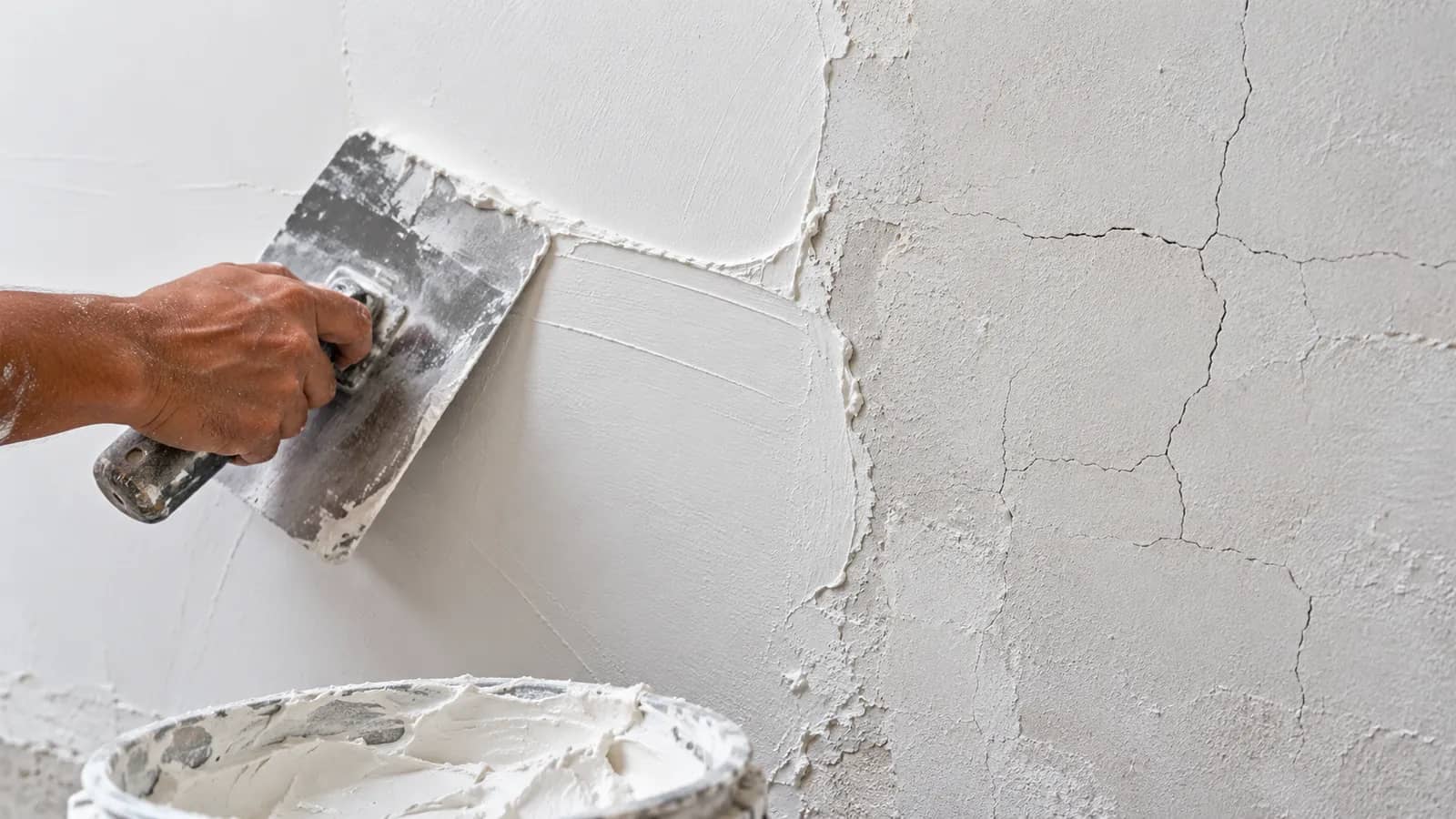 Illustration: a steel trowel spreading smooth white wall putty next to an older patch with fine shrinkage cracks